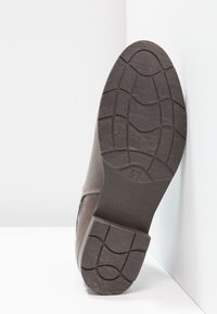 Semelle de chaussure marron montrant un caoutchouc texturé avec un motif de relief et un talon carré, arborant une indication de taille 37 estampillée sur le côté.