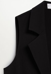 Gros plan sur un blazer noir sans manches avec un col à revers cranté, présenté sur un fond blanc uni.