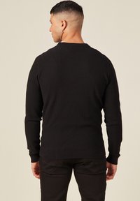 Schwarzer Strickpullover mit langen Ärmeln, geribbelter Textur und Rundhalsausschnitt. Die Rückansicht zeigt ein tailliertes Design und minimale Details.