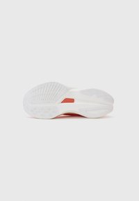 Suela de zapatilla blanca con acentos rojos, bandas de goma texturizadas y una forma suave y redondeada. Se pueden ver surcos notables y patrones circulares.