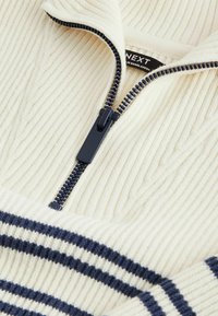 Suéter de punto color crema con un cuello de media cremallera, que presenta una textura acanalada y franjas de color azul marino en la parte inferior.