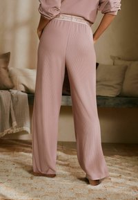 Gaiši rozā, ribota auduma plaša stila bikses ar zīmola elastīgu jostasvietu. Audums ir maigs un papildina brīvu piegriezumu.