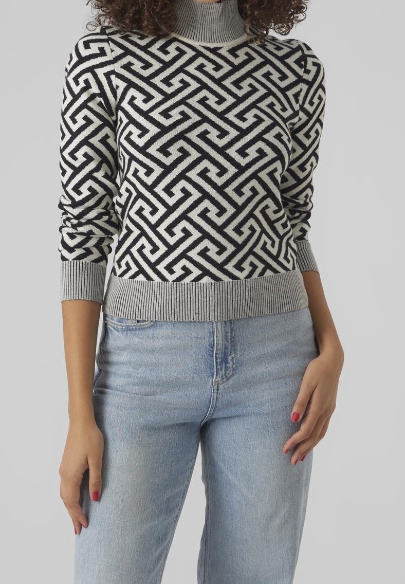 Schwarz-weiß gemusterter Pullover mit hohem Kragen, weicher Strickstruktur und gerippten Bündchen und Saum, kombiniert mit hellblauen Jeans.