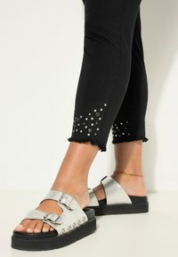 Pantalones cortos negros con el dobladillo deshilachado, decorados con tachuelas plateadas. Sandalias de plataforma plateadas con dobles hebillas y tachuelas redondas en la suela.