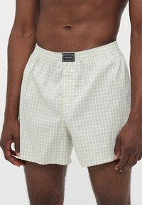 Lys grønne rutete boksershorts laget av pustende stoff har elastisk midje og en enkelt knappelukking foran.