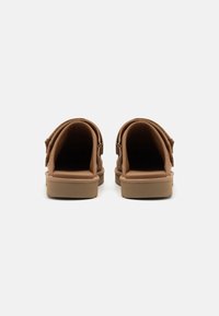 Brown open-back sandals with adjustable straps, cushioned insoles, and a textured rubber sole, featuring a minimalist design.