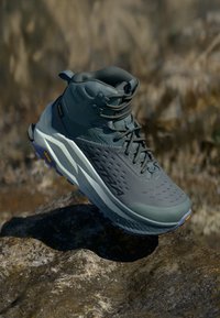 Sapatilha de trekking de cano médio em verde suave, com um upper texturizado, suporte reforçado para o tornozelo e uma sola robusta com padrões de piso distintos.