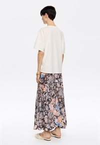 Camiseta oversize de color beige claro con mangas cortas, combinada con una falda larga y de capas con estampado floral que presenta varios colores y un diseño con pliegues.