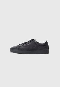 Schwarze Sneaker mit einer glatten Lederkappe, strukturierten Seitenpanelen, flachen Schnürsenkeln und einer Gummisohle. Verfügt über dezente geometrische Muster.