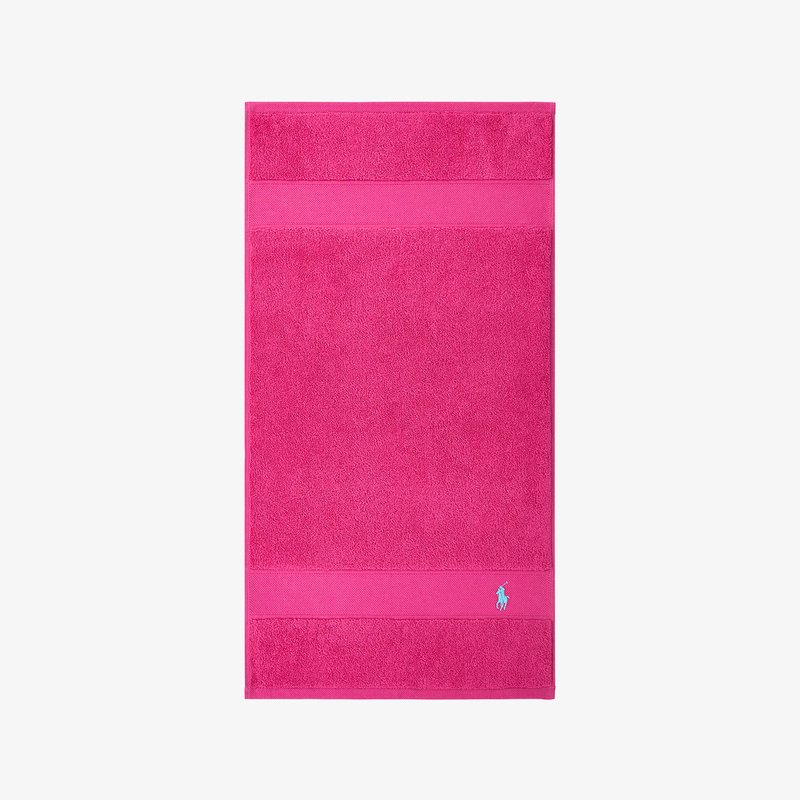 Ροζ πετσέτα μπάνιου με υφή στην επιφάνεια, που φέρει οριζόντια ταινία και ένα μικρό μπλε λογότυπο στην κάτω δεξιά γωνία.
