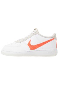 Vita lädersneakers med en framträdande orange nät Nike swoosh, grå detaljer runt vristen och en vit gummisula.