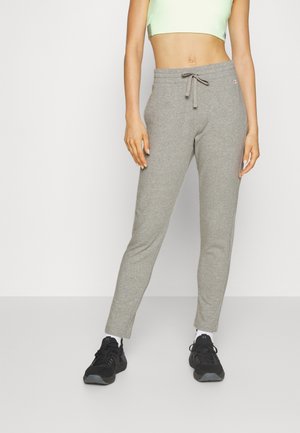 Pantalones de chándal grises hechos de una tela suave, con cintura elástica y cordón. Corte ajustado con bolsillos laterales y un pequeño parche de logo.