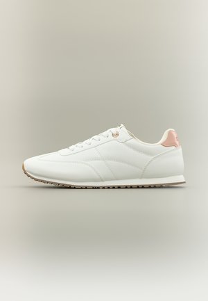 Λευκό χαμηλό αθλητικό παπούτσι με ανοιχτό ροζ ταμπελάκι στη φτέρνα, λευκά κορδόνια και μπεζ καουτσούκ σόλα σε ουδέτερο φόντο.