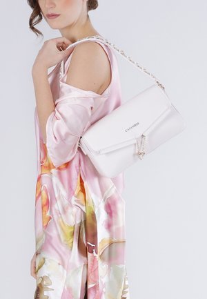 Donna che indossa un vestito in satin rosa a fiori tiene una borsa bianca da spalla con tracolla a catena e logo "CAFÉNOIR".