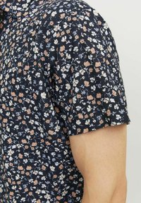 Maglietta a maniche corte, blu navy, con un motivo floreale in rosa chiaro, bianco e blu. Tessuto morbido, vestibilità relax e collo classico.