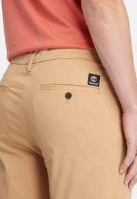 Housut Timberland khaki, joissa on takatasku mustalla logo-täggillä ja yksi musta nappi. sileä kangas, jossa on räätälöity istuvuus.