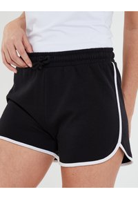Shorts noirs à taille élastique avec des bordures blanches, dotés d'un cordon de serrage. Le tissu semble doux avec une coupe décontractée et de légers fentes latérales pour le mouvement.