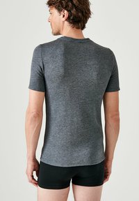 Camiseta gris de manga corta hecha de una tela texturizada, con cuello redondo y un estilo ajustado, vista desde la parte de atrás.
