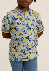 Polo shirt met een patroon van gele, blauwe en groene vruchten en bladeren. Korte mouwen, marineblauwe kraag en accentafwerkingen. Gestructureerde textuur.