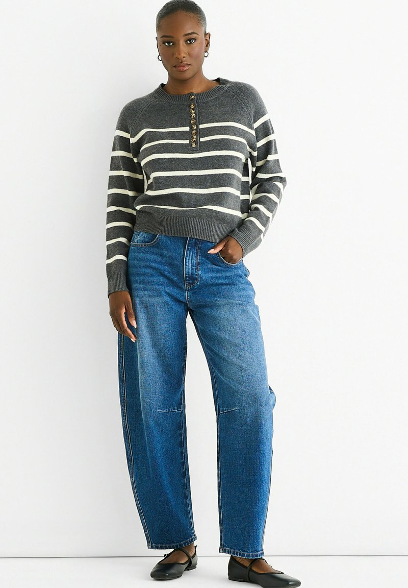 Gray and white striped sweater with a round neckline and button detail, paired with loose blue denim jeans. Black flat shoes complete the outfit.