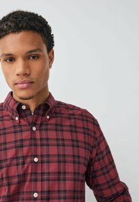 Rot- und schwarzkariertes Hemd mit Button-Down-Kragen, ausgestattet mit weißen Knöpfen und einem kleinen blauen Logo auf der Brust. Aus Baumwollmaterial, lässige Passform.