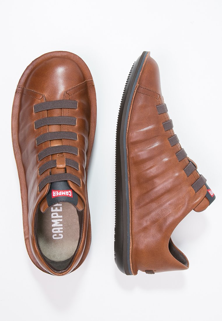 Brown leather sneakers with elastic straps, rounded toe, textured side panels, and a black rubber sole. Camper logo on the tongue.