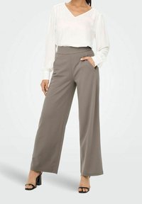 Lichte witte blouse met V-hals, gecombineerd met hoge, brede grijze broek met zijzakken, gedragen met zwarte hakken.