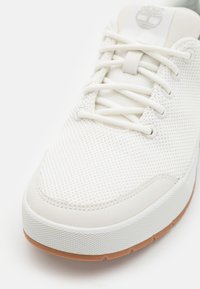 Fehér sneaker lélegző hálós felsőrésszel, sima bőr kiegészítőkkel, gumitalppal és azonos színű fűzőkkel. Diszkrét márkajelzés található az nyelvén.