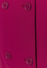 Manteau fuchsia présentant une texture lisse, un design croisé et des boutons en plastique brillants. Détail de couture visible le long de la couture.