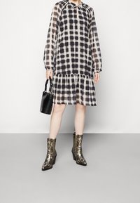 Robe à carreaux noir et blanc translucide avec des manches longues, un ourlet froncé et un col à nouer. Assortie à des bottes à imprimé serpent dorées et un sac noir.