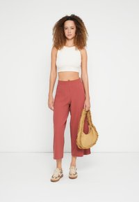 Apgriezts balts tanktops, rūsas krāsas platkāju bikses, bēša rakstainas sporta kurpes un dzeltenbrūna rokassomiņa ar volānu maliņu.