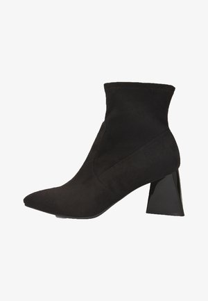 Stivale alla caviglia nero in suede, con punta appuntita e tacco scolpito nero. La parte superiore presenta una silhouette aderente e elasticizzata.