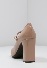 Beige lackläder högklackad sko med rund tå, midjeband och kraftig klack. Slät yta med sömnadsdetaljer.