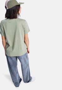 Olivově zelené bavlněné tričko spárované s volnými, světle modrými džíny a bílými teniskami. Osoba nosí khaki čepici s růžovým akcentem.