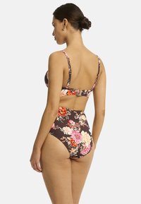 Modello di spalle, che indossa un bikini a stampa floreale con sfondo marrone, che mostra una parte inferiore alta e spalline regolabili.