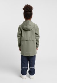 Giacca verde con cappuccio e vestibilità ampia, polsini elasticizzati e striscia riflettente all'orlo, abbinata a pantaloni blu navy con due bande riflettenti.