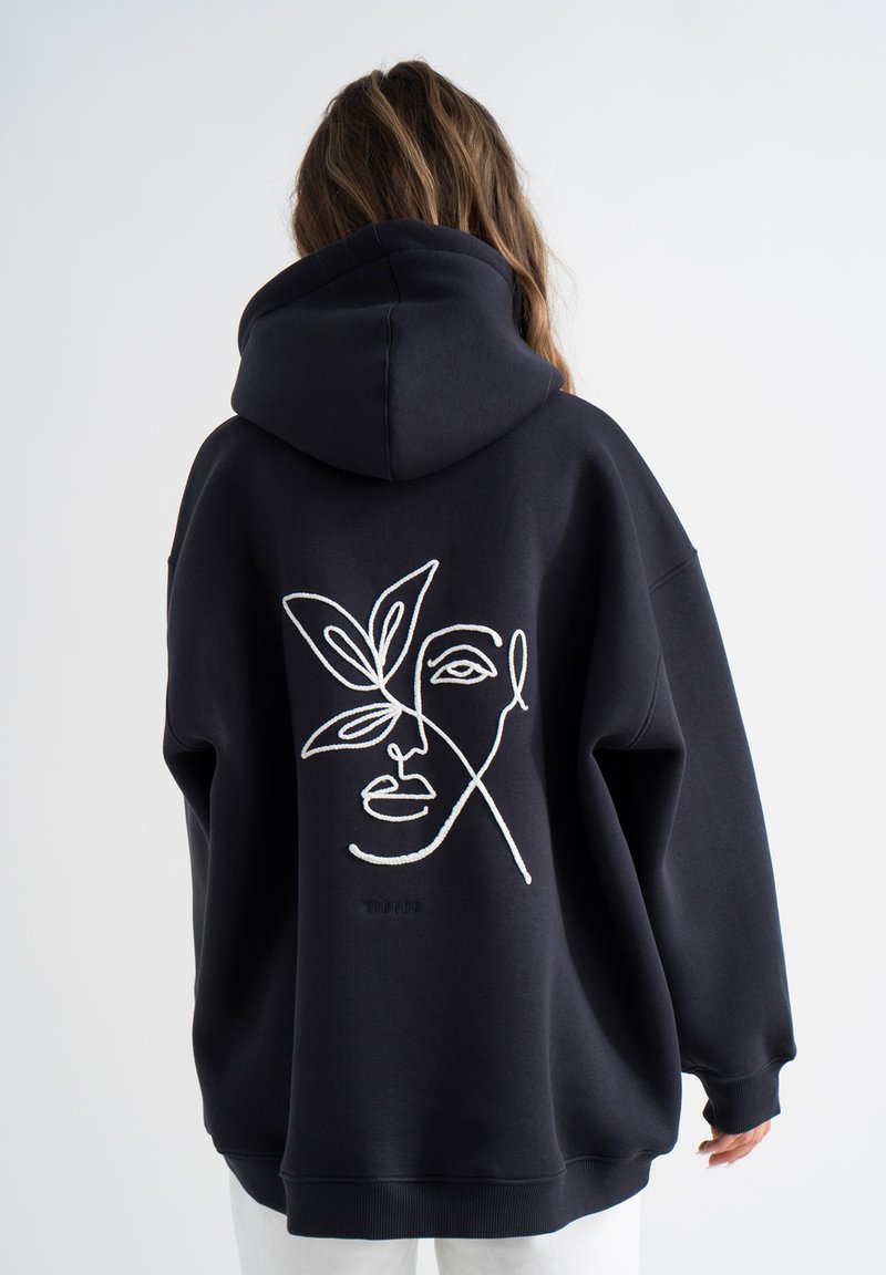 Marineblauwe oversized hoodie met een witte geborduurde gezicht- en bladerenontwerp op de achterkant, met een capuchon met trekkoord en ribbelmanchetten.