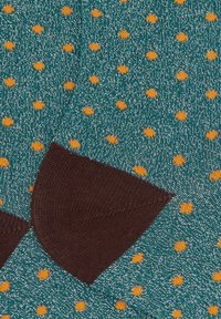 Calze lavorate a maglia color teal con pois arancioni, caratterizzate da un polsino a costine marrone e un leggero scintillio dovuto ai fili metallici.