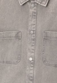Veste en jean grise avec col, deux poches plaquées devant, et boutons-pression métalliques au centre.