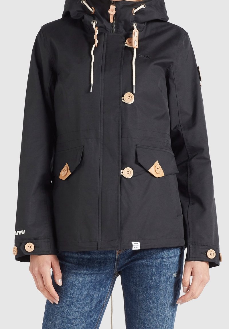 Veste noire imperméable avec capuche, boutons en bois brun clair, accents à cordon de serrage et deux poches avant avec rabats.