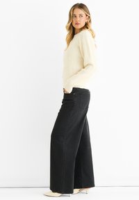 Cream ribbed knit sweater with round neck and textured finish, paired with high-waisted wide-leg black jeans. Beige pointed heels complete the look.