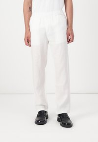 Pantaloni bianchi in lino con vita elasticizzata, vestibilità rilassata e tessuto leggermente strutturato, abbinati a mocassini neri.