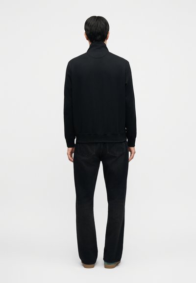 Μαύρο φούτερ με ψηλό γιακά, εφαρμοστά μανίκια και τελείωμα, σε συνδυασμό με σκούρο τζιν και casual παπούτσια με υφασμένη σόλα.