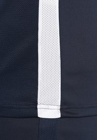 Close-up of dark blue and white mesh fabric with vertical white stripe and visible stitching at the seam.