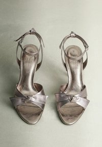 Metallic silver high-heeled sandals with a knotted front strap and ankle strap, showcasing a smooth, shiny texture and open toe design.