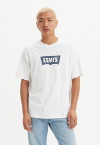 Balta medvilnė t-marškiniai su tamsiai mėlynu Levi's logotipu ant krūtinės; laisvas kirpimas, trumpomis rankovėmis, apvaliu iškirpimu ir švelniu audiniu.