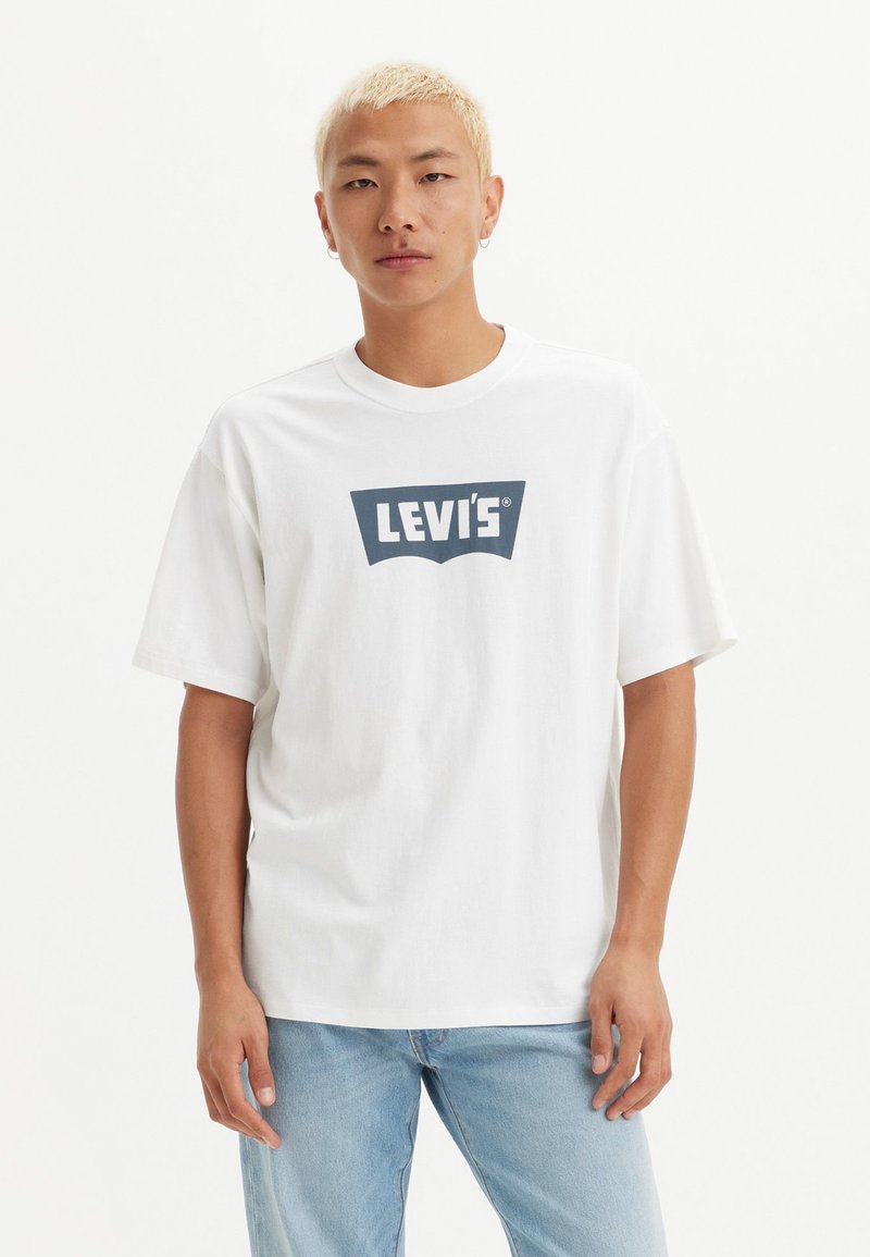 Balta medvilnė t-marškiniai su tamsiai mėlynu Levi's logotipu ant krūtinės; laisvas kirpimas, trumpomis rankovėmis, apvaliu iškirpimu ir švelniu audiniu.
