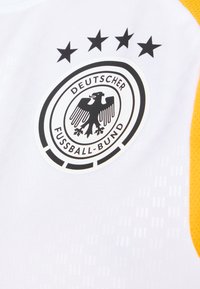 White athletic shirt with yellow accents, featuring a black and white German Football Association logo and four black stars above it.