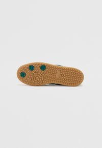 Sneaker sole featuring a textured rubber surface in beige with a zigzag pattern, three green circular accents, and branded detail.
