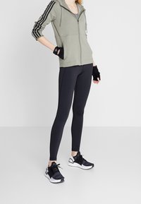 Grön zip-up hoodie med grå foder, svarta leggings och svarta träningsskor med vita sulor, med tre svarta ränder på ärmarna.